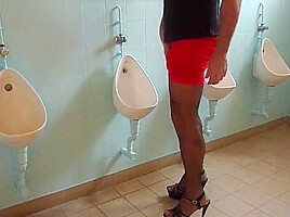 Male slut in tranny masturbates on a urinal