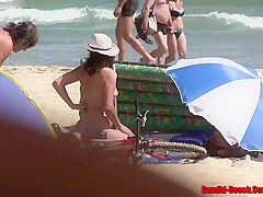 Naked woman is enjoying on the beach while people are staring at her trimmed pussy